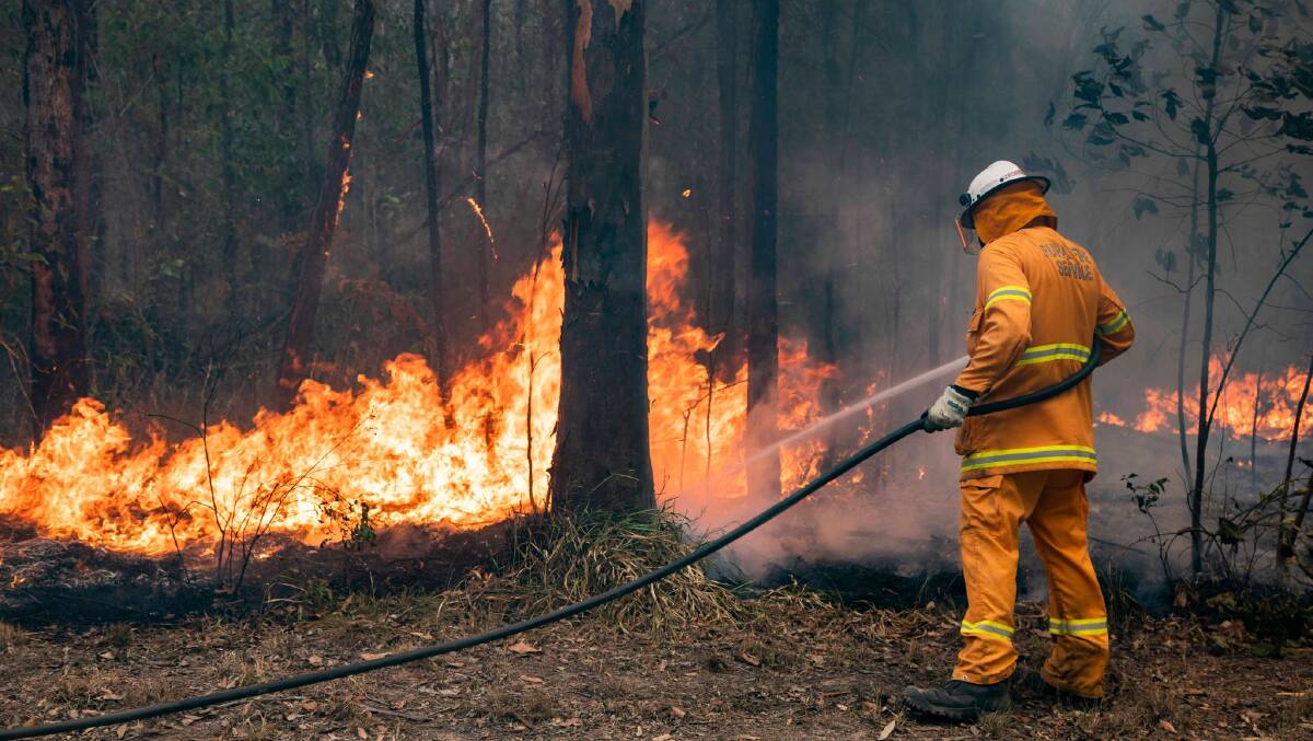 A firefighter stands with his back to the camera putting out a bush fire. Picture by QFES